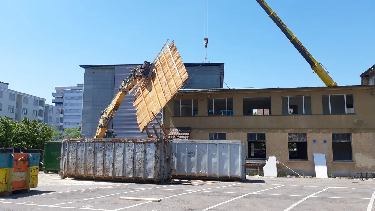 Baustelle mit Abbruchhaus, Bagger und Mulden für den Bauschutt. 